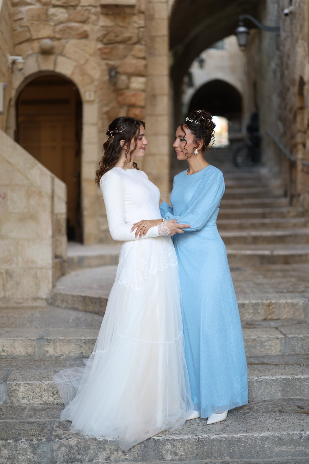 כלה ומלווה במדרגות העיר העתיקה, חצי אסוף בגלים ואסופה מתולתלת עם פרחים
